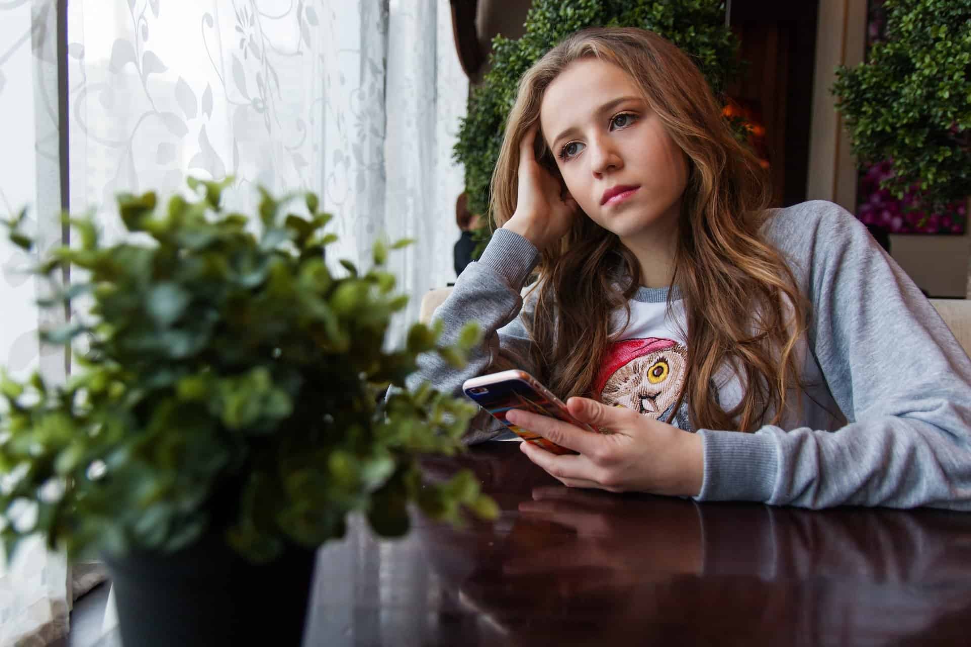 A young lady holding a phone leaning on her hand looking sad